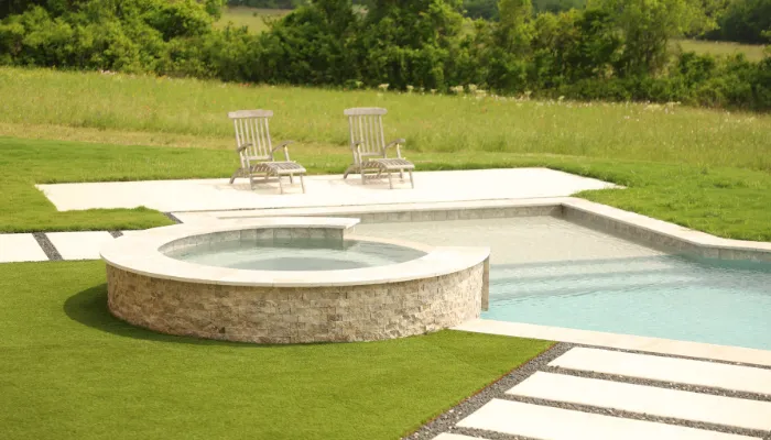 Backyard with a rectangular inground pool and a round above-ground pool, surrounded by green grass. Two lawn chairs are placed on the grass, and a paved walkway leads to the pools.