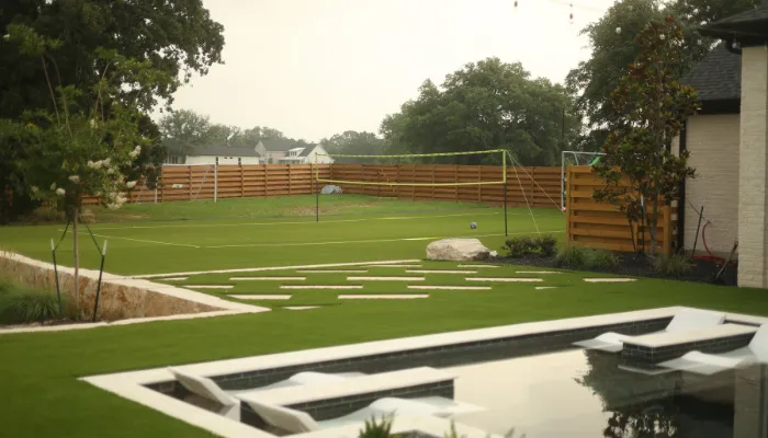 Modern backyard with pool, volleyball court, and synthetic turf lawn.